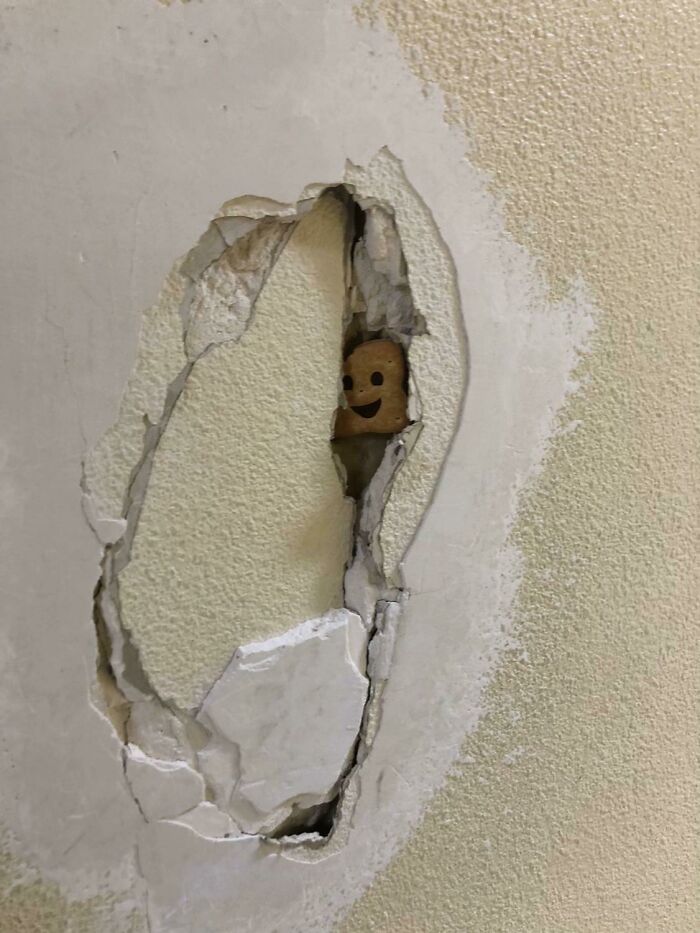 A piece of toast with a smiley face peeks through a hole in a wall, a bizarre and mysterious image.