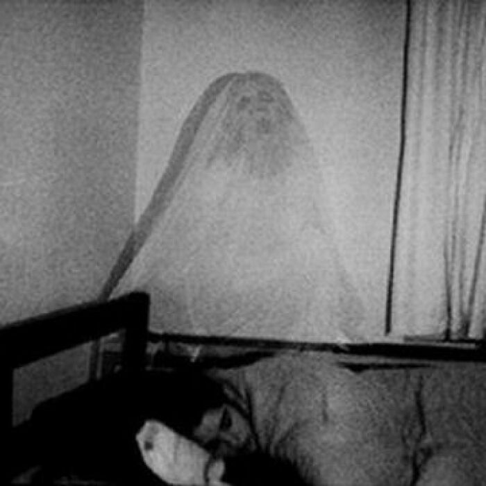 Black and white creepy photo of a ghostly figure above a sleeping person