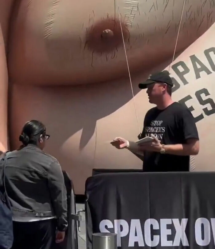 Man talking near giant Elon Musk inflatable at Times Square event