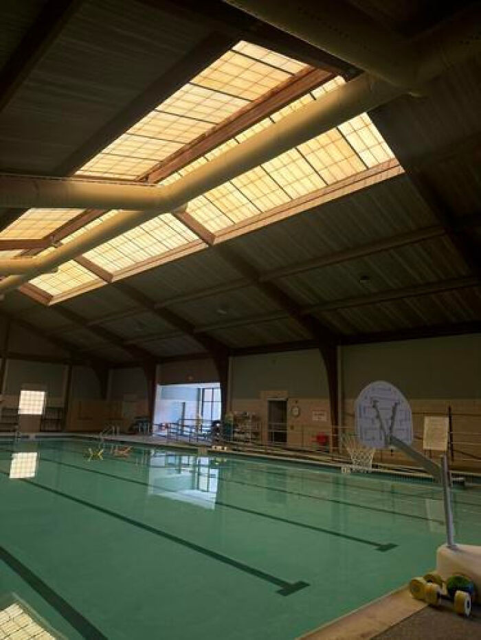 An indoor swimming pool with a high, skylit ceiling, creating a haunting liminal space.