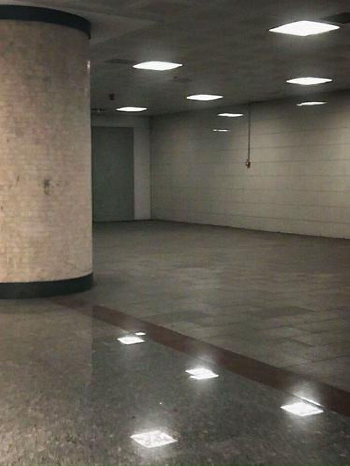 Empty, dimly lit concrete room with reflective floors and square lights, a classic liminal space.