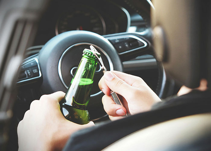 Person opening a beer bottle inside a car warning against risky life mistakes