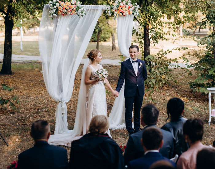 Outdoor wedding ceremony with bride and groom holding hands under floral arch