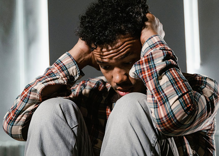 A man looking distressed, holding his head, conveying the emotion of someone whose popular high school days are behind him.