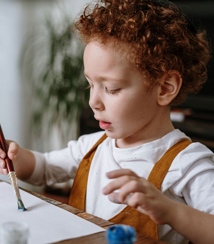 A young boy with curly red hair intently painting, a visual representation of autism and brain triggers. A young boy with curly red hair intently painting, a visual representation of autism and brain triggers.