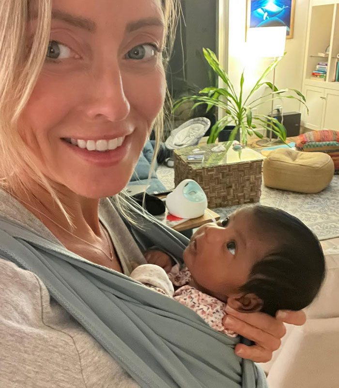 Woman smiling while holding baby in a carrier, who was born to the wrong parents after an IVF mix-up. Woman smiling while holding baby in a carrier, who was born to the wrong parents after an IVF mix-up.