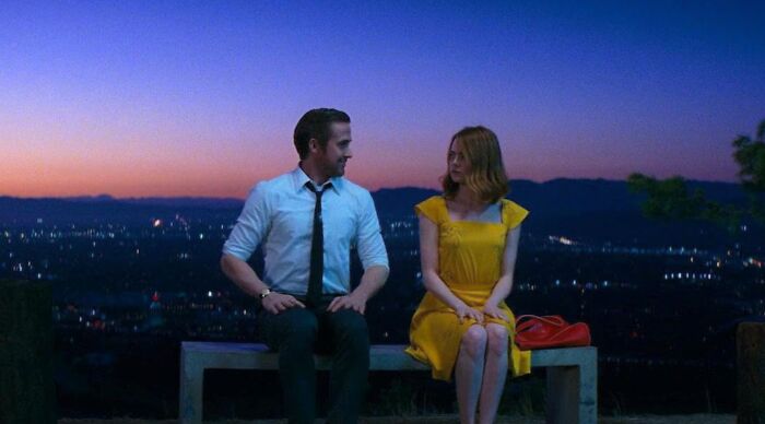 Ryan Gosling and Emma Stone sitting on a bench at night with a city view for a Popular Fiction and Movies Would You Rather Poll.