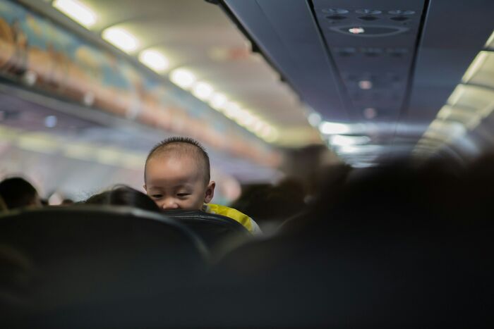 A baby peeking over a seat on a plane, showcasing plane interactions.