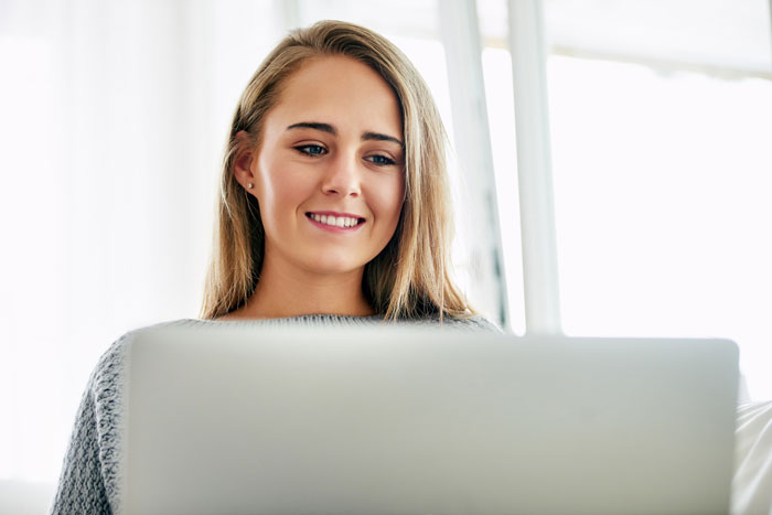 A woman smiling and looking at a laptop, representing the surprising results of DNA testing stories.