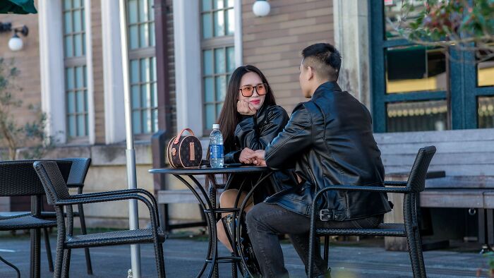 A couple sits at an outdoor cafe table, holding hands, illustrating acceptable actions on a date.
