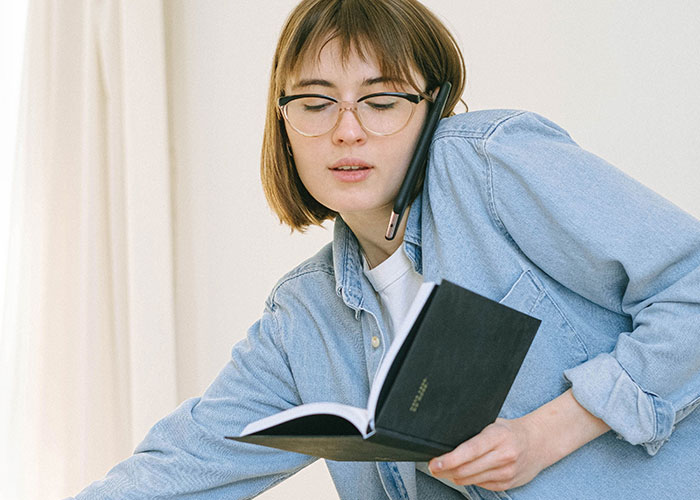 A young woman with glasses on the phone while holding a planner, symbolizing socially unacceptable advice.