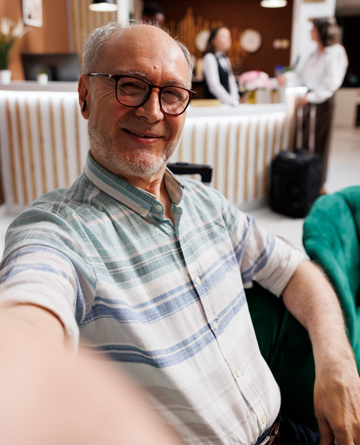 A smiling older man wearing glasses takes a selfie in a hotel lobby. This image relates to things people saw on their late parents' phones.