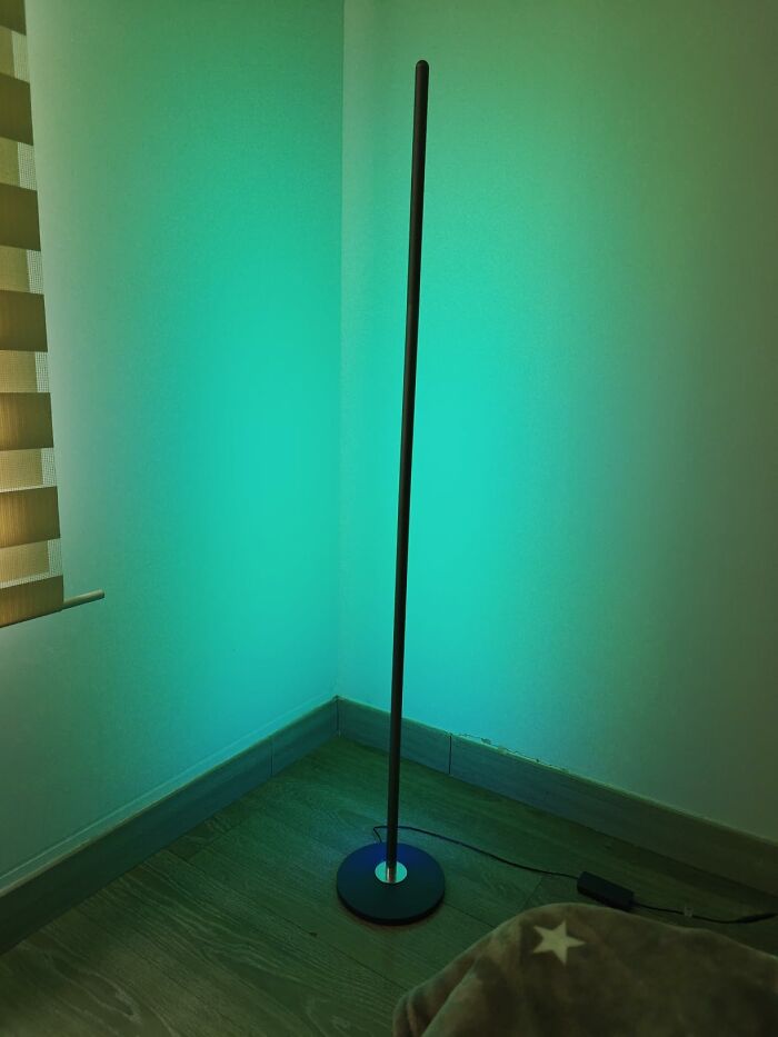 A tall, slim floor lamp casting a green glow in a corner, one of the home finds available for Prime Day.