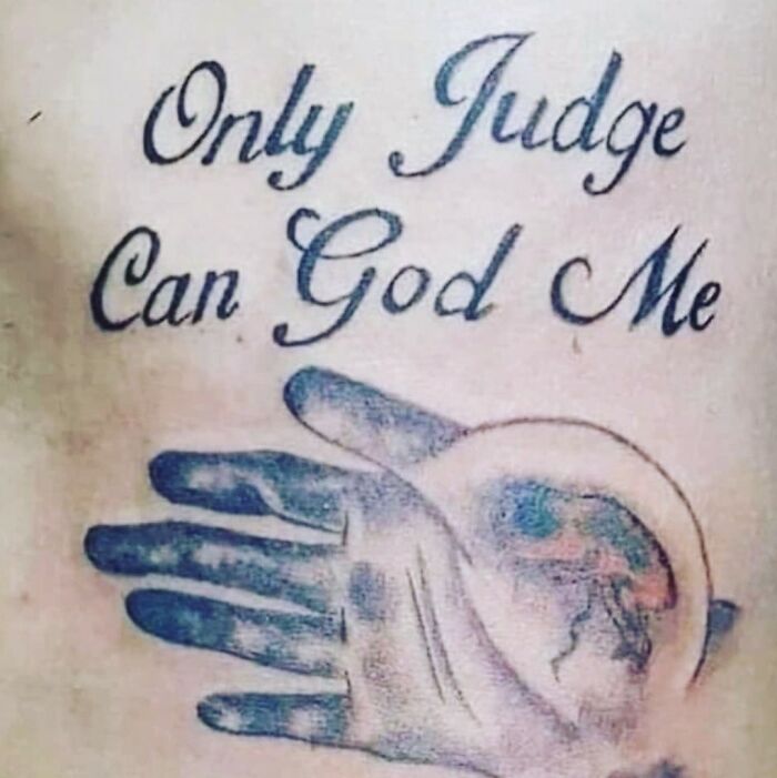 A tattoo fail with the text Only Judge Can God Me and a hand holding a globe.