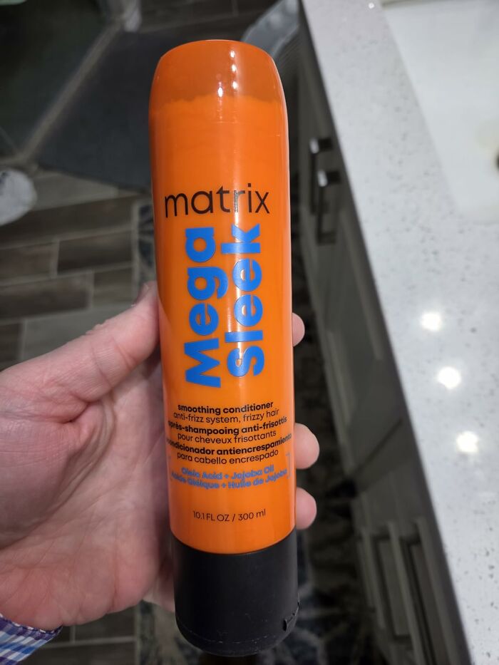 A hand holding an orange bottle of Matrix Mega Sleek smoothing conditioner, one of the Prime Day Deals for beauty products.