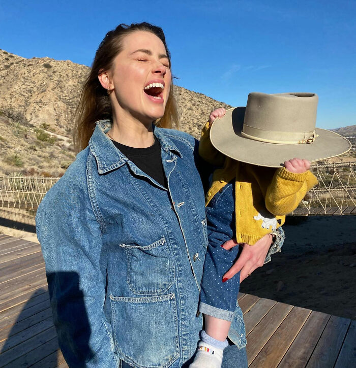 Amber Heard enjoying her new life in a new country, smiling while holding her child who wears a large hat. Amber Heard enjoying her new life in a new country, smiling while holding her child who wears a large hat.