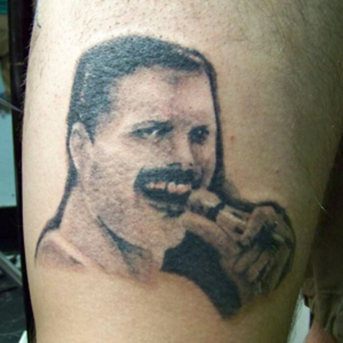 Hilarious tattoo fail meme of a poorly rendered black and white portrait tattoo of Freddie Mercury singing into a microphone.