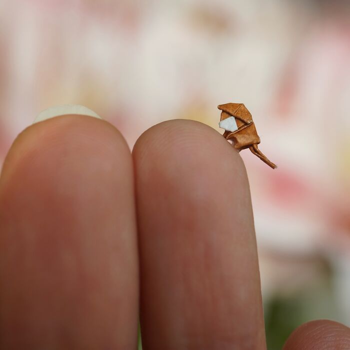 Tiny paper figure of a bird perched on a fingertip, demonstrating immense detail.