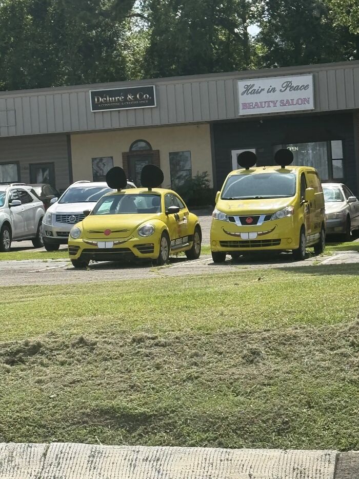 A bizarre image of two yellow cars with Mickey Mouse ears and cartoon faces parked outside a beauty salon.