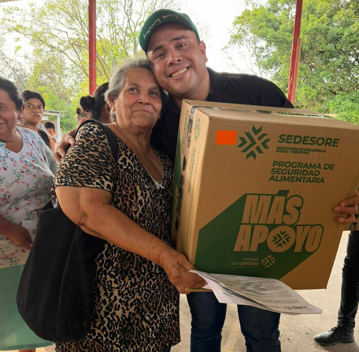 A mayor with an elderly woman holding a box, amidst the Good-Vibe Girls viral controversy and Father's Day party.