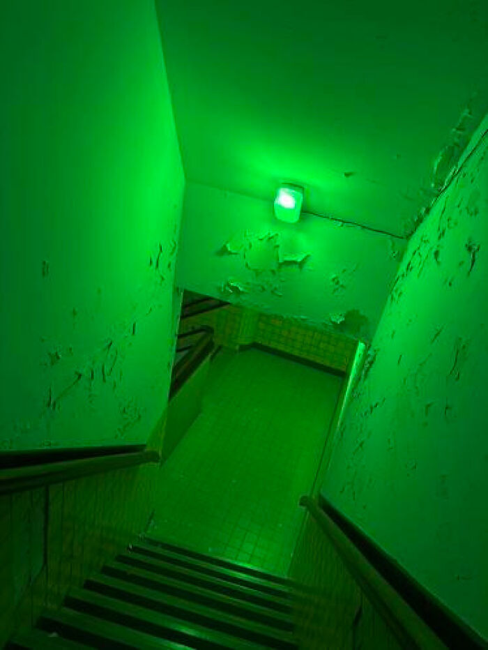 Stairwell with peeling green paint and eerie green lighting, a haunting liminal space.