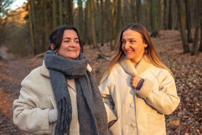 Two women warmly dressed chatting and walking in autumn forest