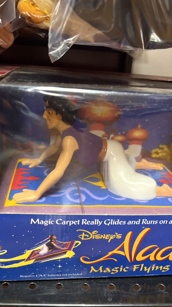 A bizarre image of an Aladdin action figure on a magic carpet, posed in an unusual way, still in its packaging.