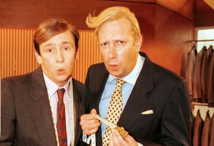 Two men in suits with measuring tape in clothing store
