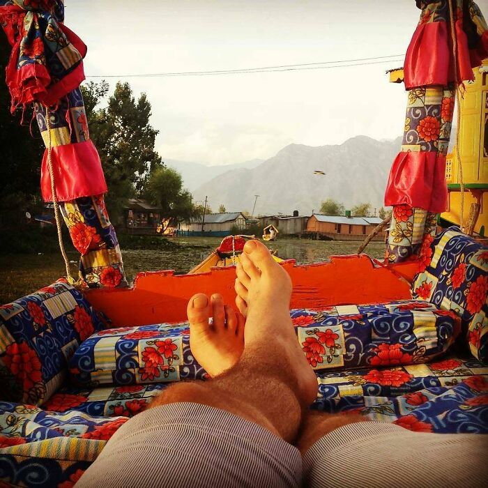 Feet resting on a colorful boat on a lake with mountains in the background, a serene escape from unsolved mysteries.