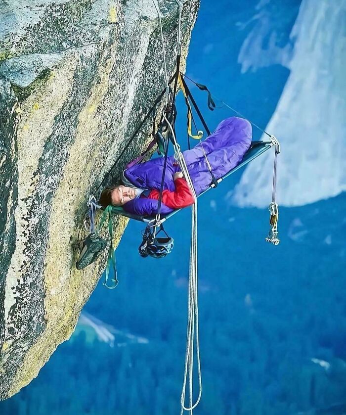 Climber sleeping in hanging purple bivy tent on steep mountain cliff
