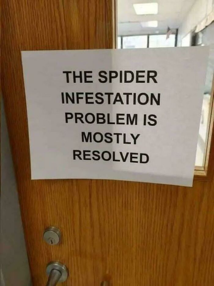 Sign on wooden door stating spider infestation problem mostly resolved