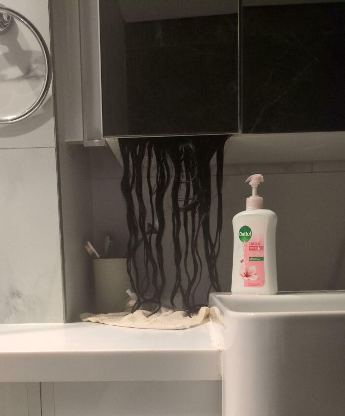 Shadow resembling black tendrils cascading from bathroom cabinet near sink