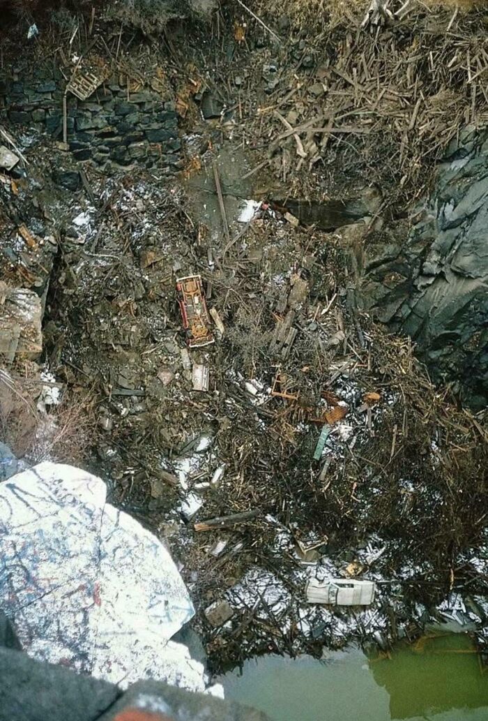 Debris and wreckage piled in deep ravine surrounded by rocky terrain and branches