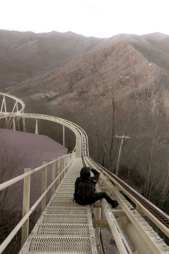 Person photographing abandoned roller coaster track in urban exploration site