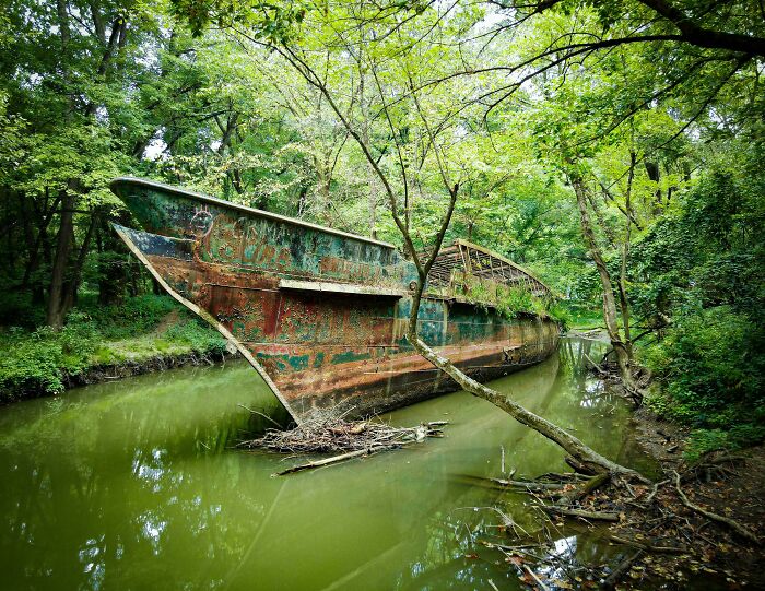 Rusty abandoned ship in forest creek surrounded by trees urban exploration