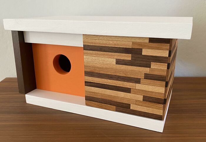 Creative birdhouse with multi-wood design and orange circular entrance hole