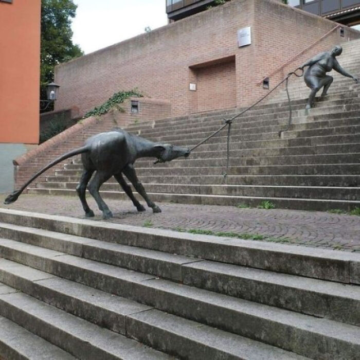 Creative sculpture of a dog pulling a person up stairs showcasing designer genius