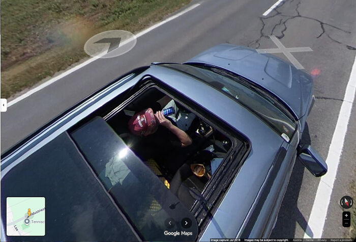 Bizarre funny screenshot of Google Maps image showing man drinking in car through sunroof