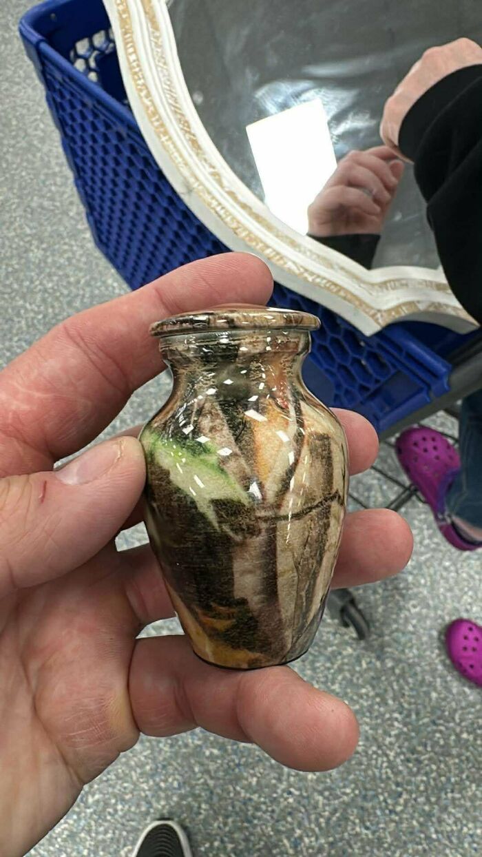 Small decorative urn with camouflage pattern held in hand at Goodwill