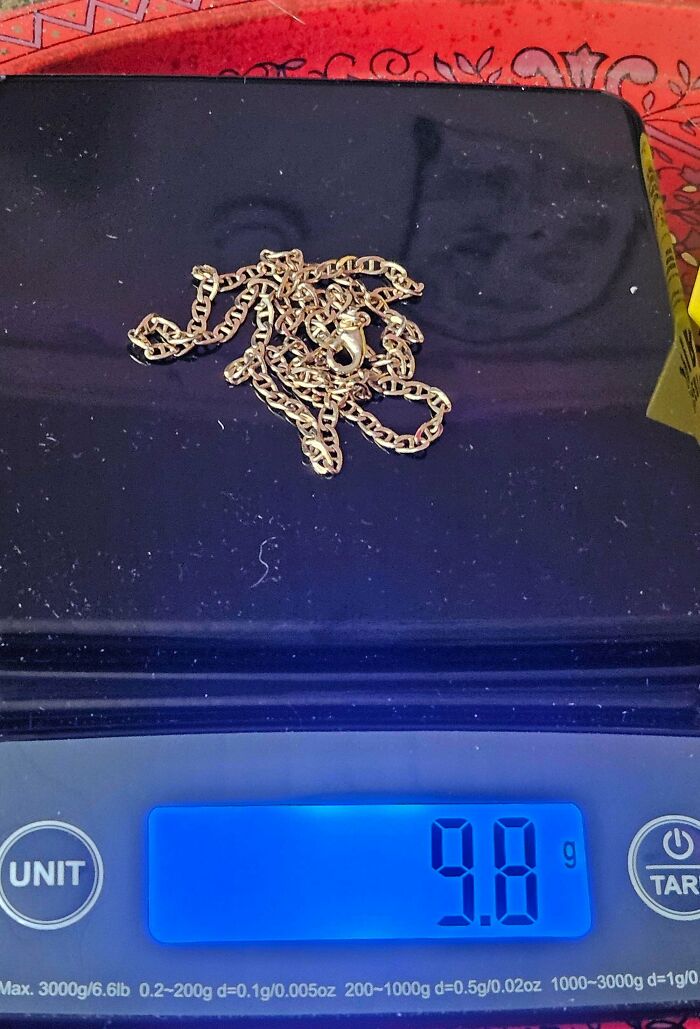 Gold chain necklace being weighed on digital scale showing 9.8 grams