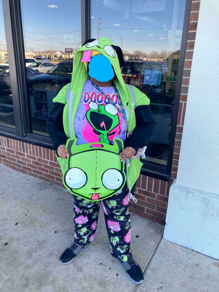 Person dressed in green cartoon-themed outfit holding matching handbag outside store