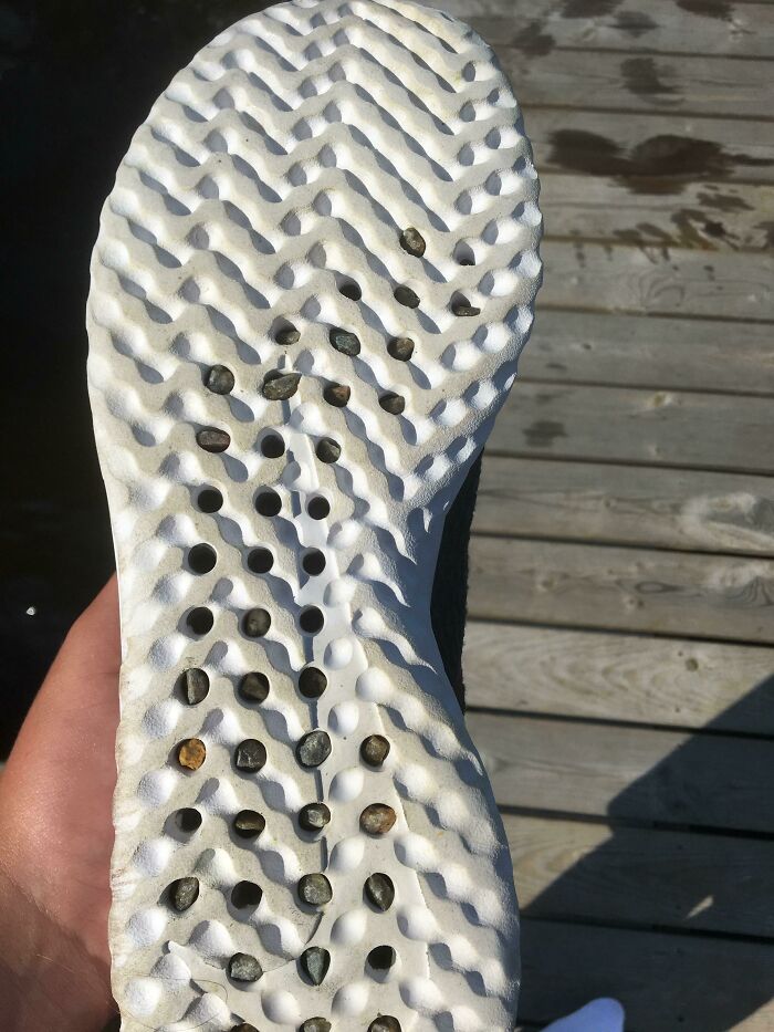 The sole of a shoe with numerous small pebbles stuck in the holes, indicating a flawed clothing design.