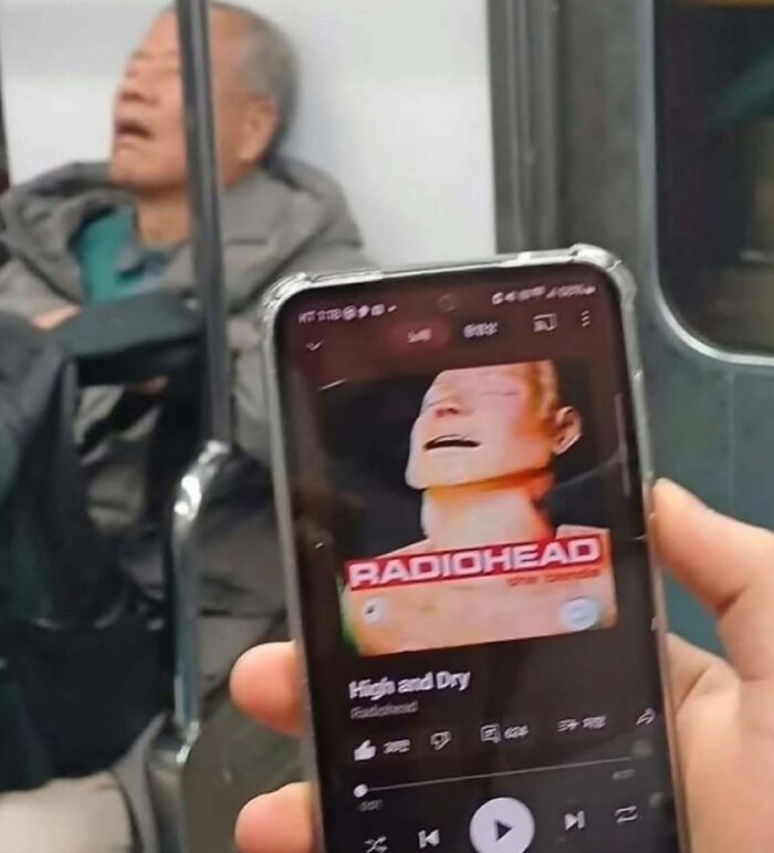 Person holding phone playing Radiohead music on subway with sleeping passenger