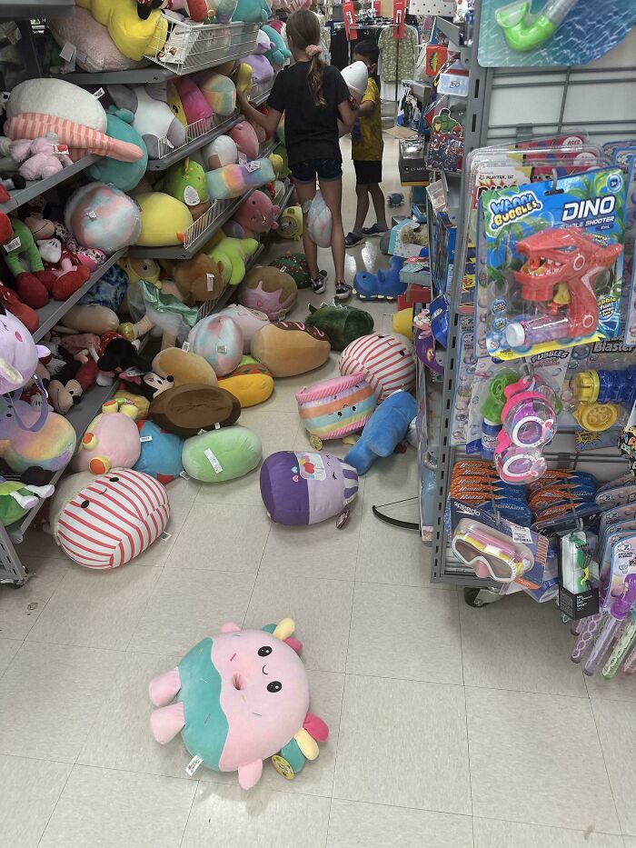 Messy retail store aisle with plush toys scattered and kids shopping inside
