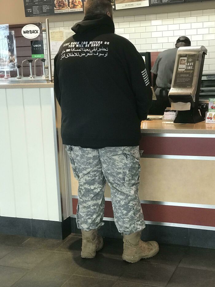Person wearing a hoodie with threatening text about staying back 100 meters