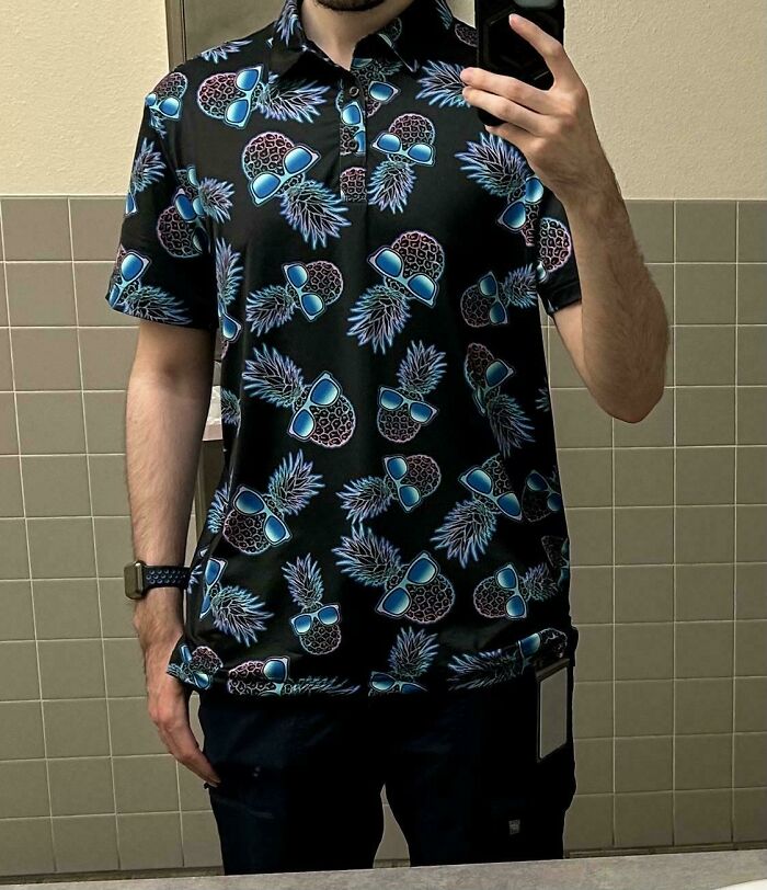 A person wearing a black polo shirt with numerous pineapple and sunglasses patterns, showcasing bad clothing designs.