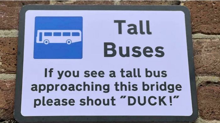 Comical tall buses sign advising to shout duck at bridge