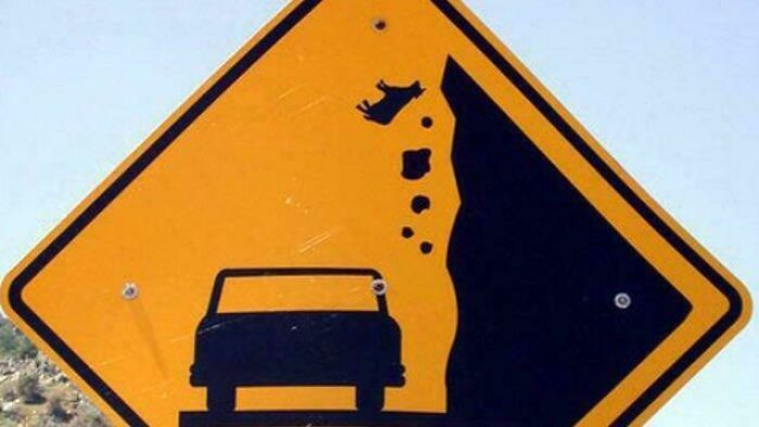 Funny road sign showing car falling off cliff with cow in air