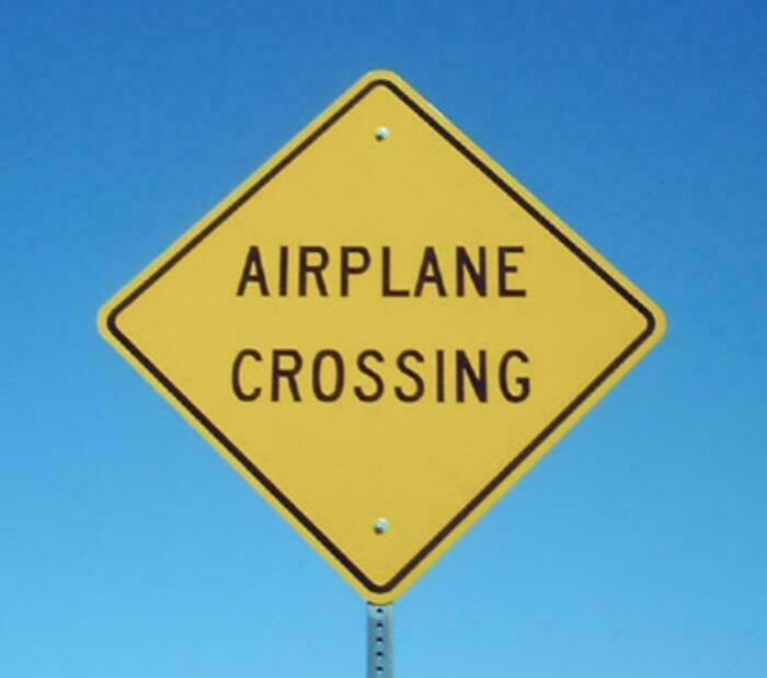 Yellow diamond-shaped airplane crossing warning sign against blue sky