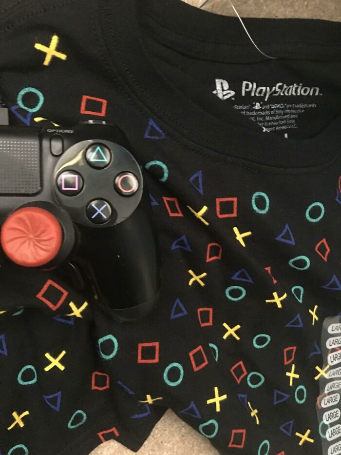 A black t-shirt featuring a repeating pattern of PlayStation symbols next to a PlayStation controller, an example of a poor clothing design.